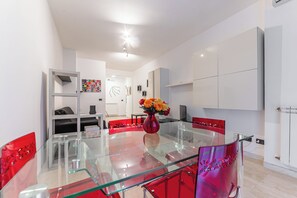 Una cocina moderna con armarios blancos, una mesa de comedor de vidrio y un jarrón rojo con flores.