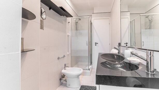 Een moderne badkamer met een douchecabine van glas, een wit toilet, een zwarte wastafel met een marmeren blad en een grote spiegel.