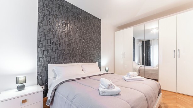 Une chambre moderne avec un mur à motifs, un grand lit avec une tête de lit, une table de chevet avec une lampe et une armoire avec un miroir.