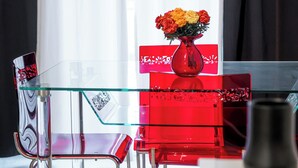 Une pièce moderne avec une table en verre, des chaises rouges et un vase rempli de fleurs.