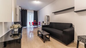 Un salon moderne avec un canapé noir, une petite table basse et un coin repas comprenant des chaises rouges et une table blanche.