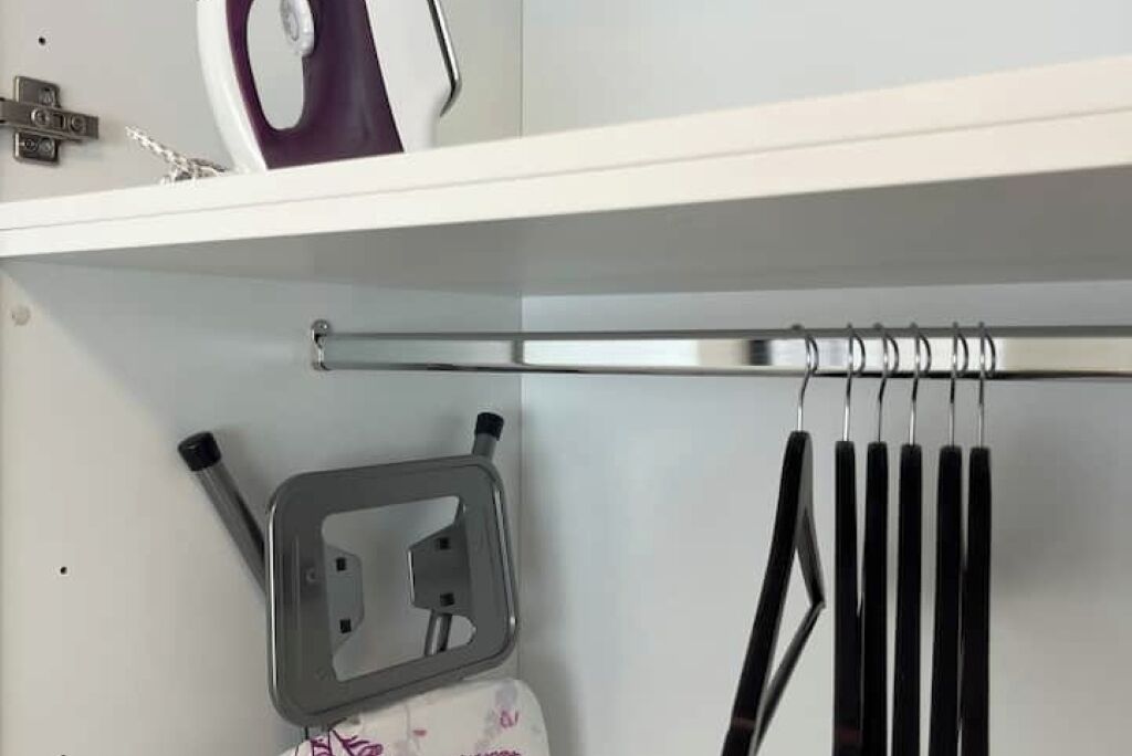 Een witte plank met een witte stoomstrijkijzer, een zwarte stoomstrijkijzer en een metalen rek met zwarte handgrepen.
