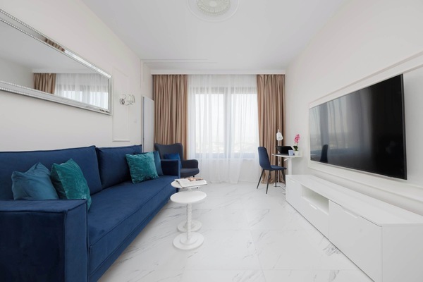 A long, navy blue velvet sofa stretches across the living area, accented by teal cushions and situated opposite a sleek white media console.