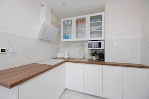 Une cuisine moderne avec des meubles blancs, un plan de travail en bois, un four à micro-ondes encastré et une machine à café.