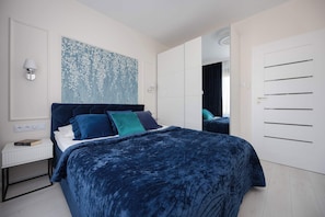 Une chambre à coucher avec un grand lit, une table de chevet, une lampe fixée au mur et un grand tableau abstrait.