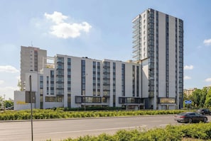Un immeuble à plusieurs étages doté d’une architecture moderne, caractérisé par un mélange de façades en verre et en béton, et un espace de stationnement situé à l’avant.