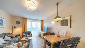 Ett modernt vardagsrum med en soffa, ett matbord och stolar. Det finns ett fönster med gardiner, en klocka på väggen och en lampa.