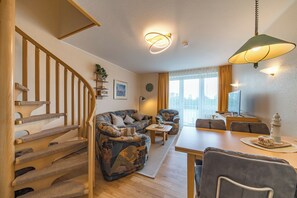 Ein Wohnzimmer mit Treppe, einer Sofagarnitur, einem Esstisch und einer Lampe.