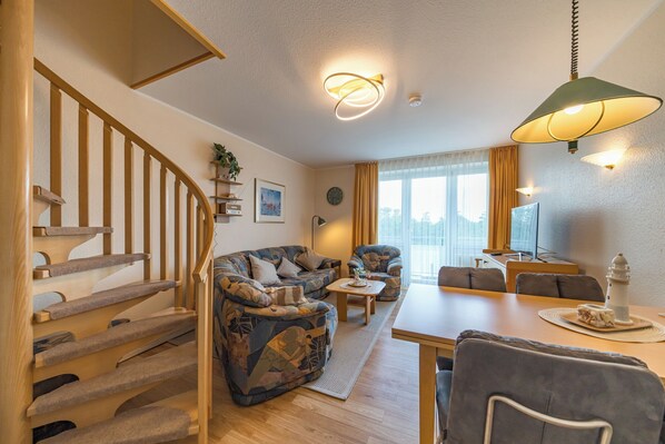 A living room with a staircase, a sofa set, a dining table, and a lamp. - Family-friendly maisonette on the North Sea with balcony and beach access (Nordseeheilbad Schillig)