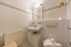 A bathroom with a white sink, mirror, toilet, and towel rack. - Family-friendly maisonette on the North Sea with balcony and beach access (Nordseeheilbad Schillig)