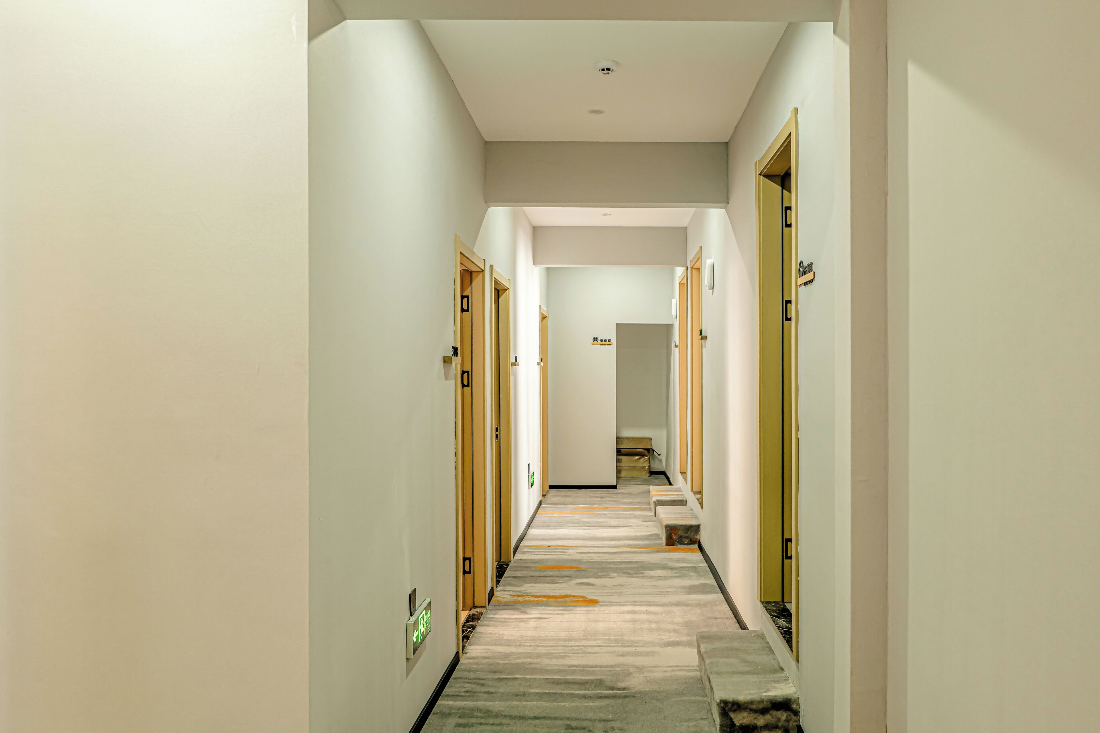 En hotels korridor med døre på begge sider, et tæppe på gulvet og et skilt, der viser vejen til elevatoren.