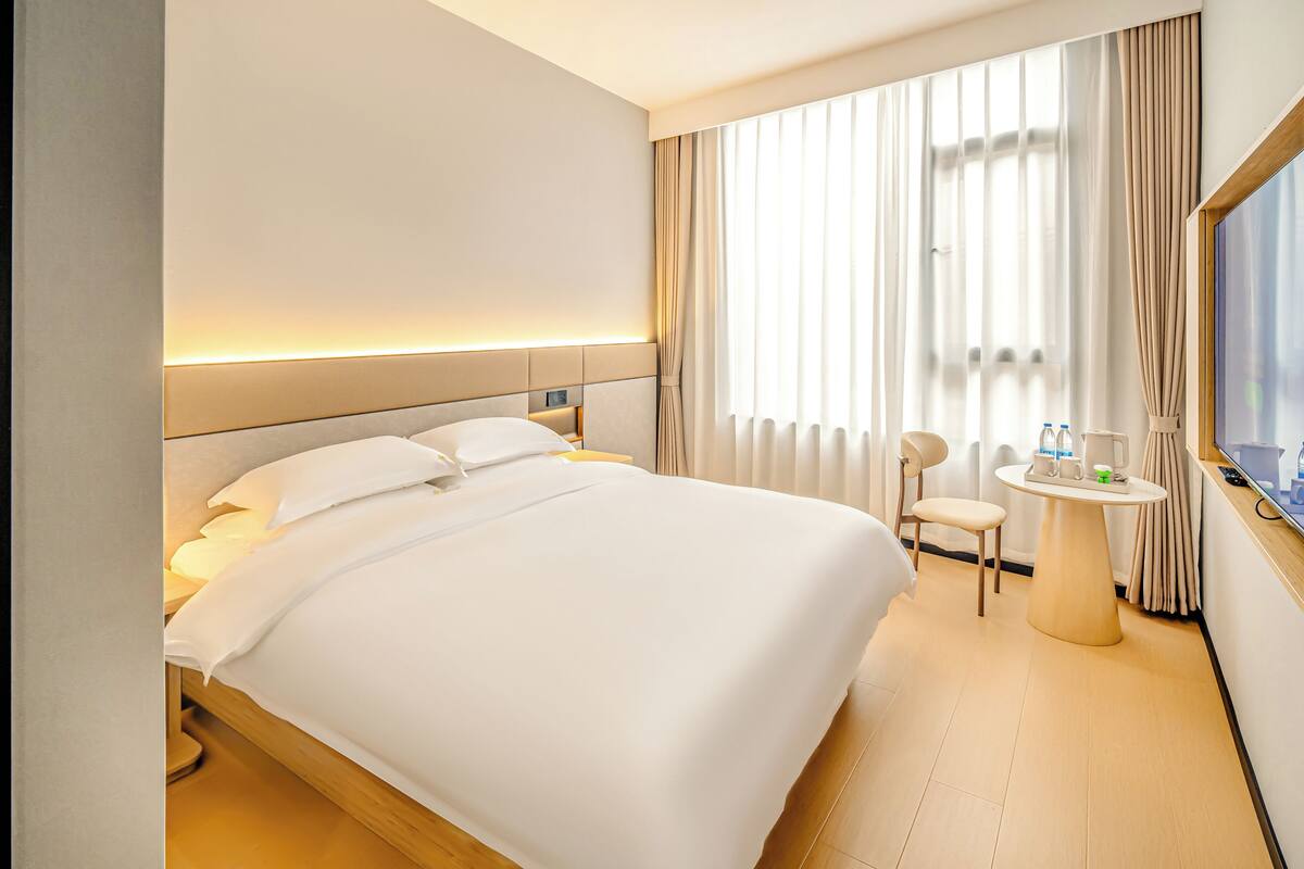 A hotel room with a bed, bedside table, chair, and a small round table with a lamp.