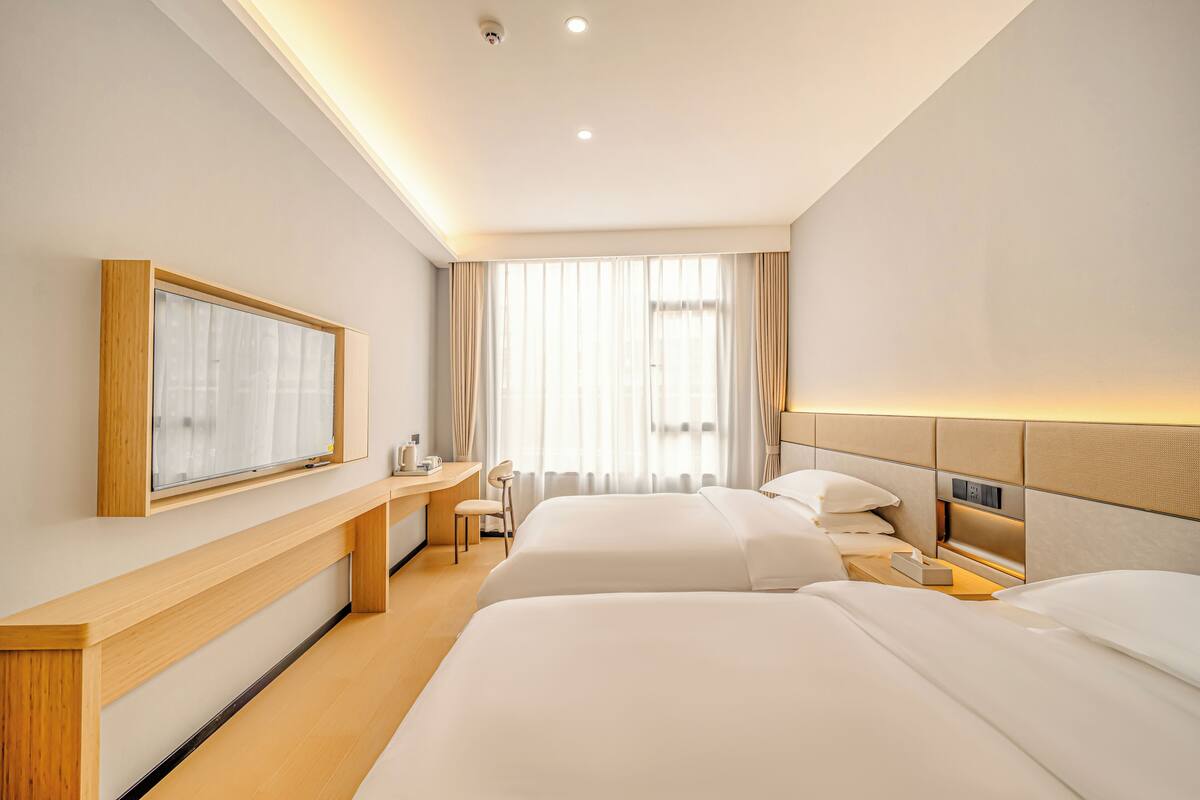 A hotel room with two beds, a desk, a chair, a TV, and a window with curtains.