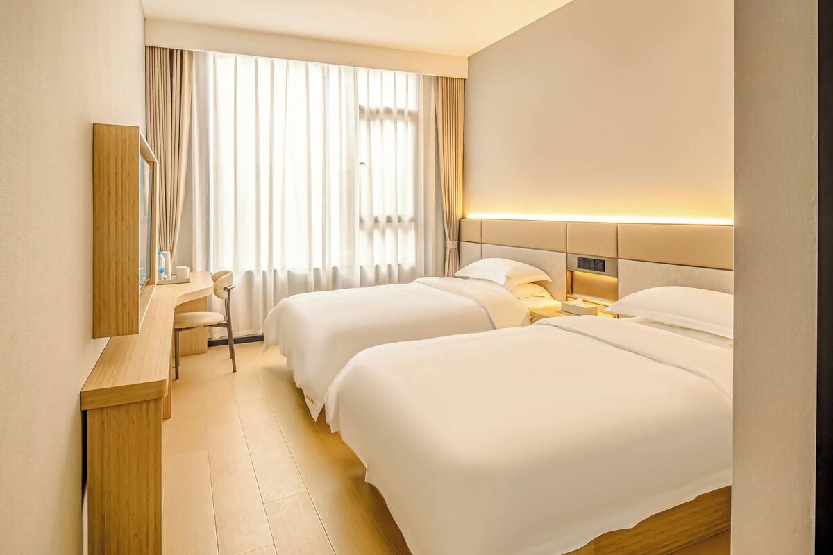 A hotel room with two beds, a desk, a chair, a mirror, and a window with curtains.