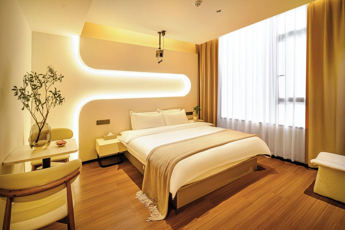 A modern hotel room with a large bed, bedside tables, a desk, and a window with curtains.