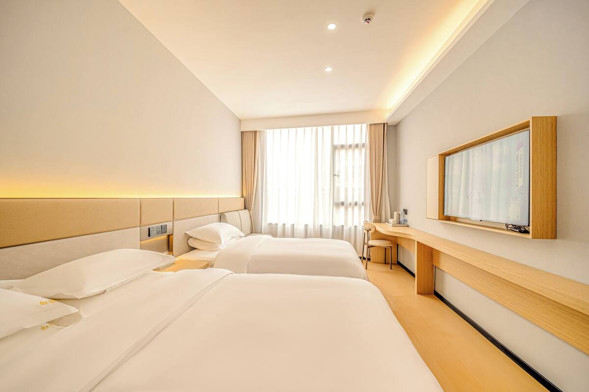 A hotel room with two beds, a desk, a television, and a window with curtains.