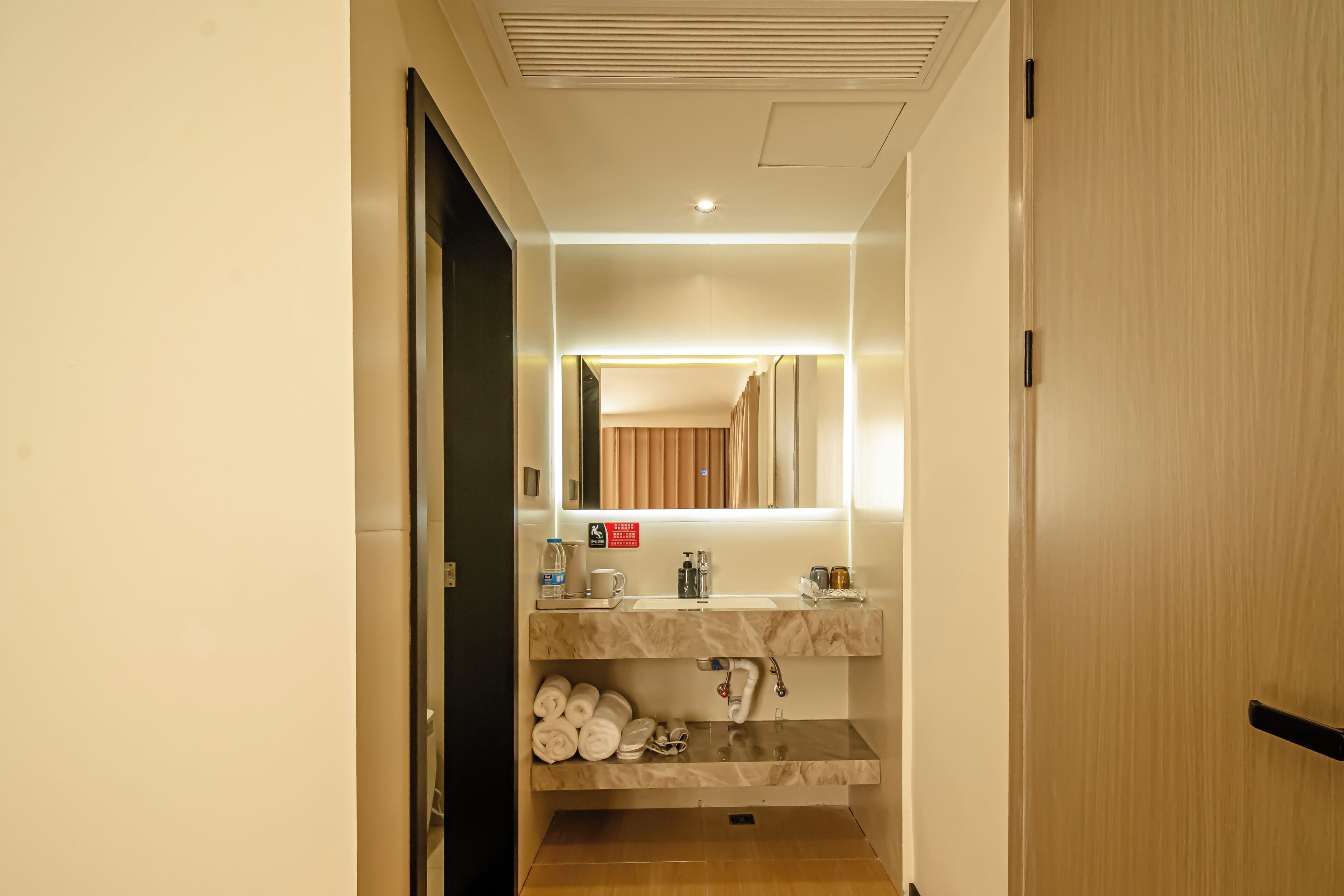 A hotel bathroom with a sink, mirror, towel rack, and a shower area.