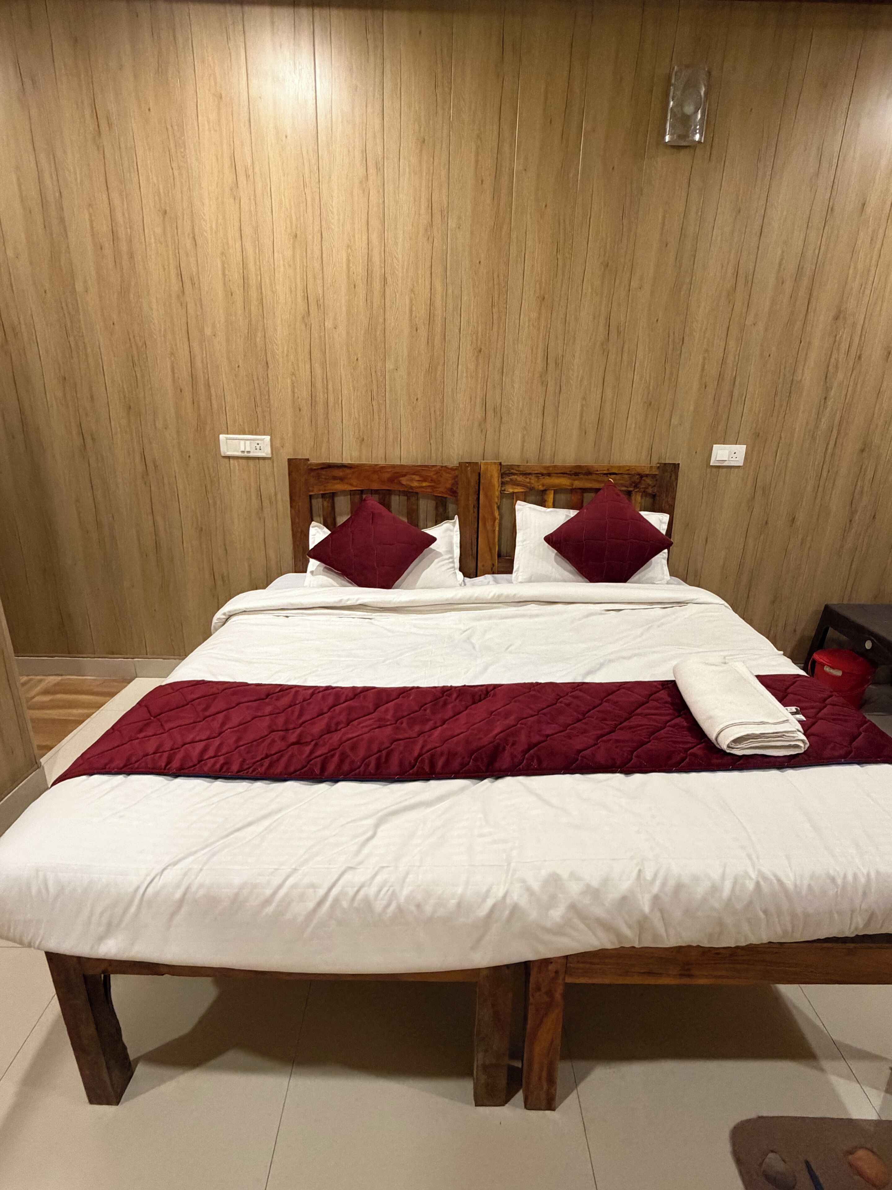 A bed with a wooden headboard, white bedding, and a red quilted blanket.