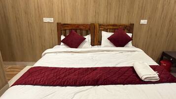 A bed with a wooden headboard, white bedding, and a red quilted blanket.