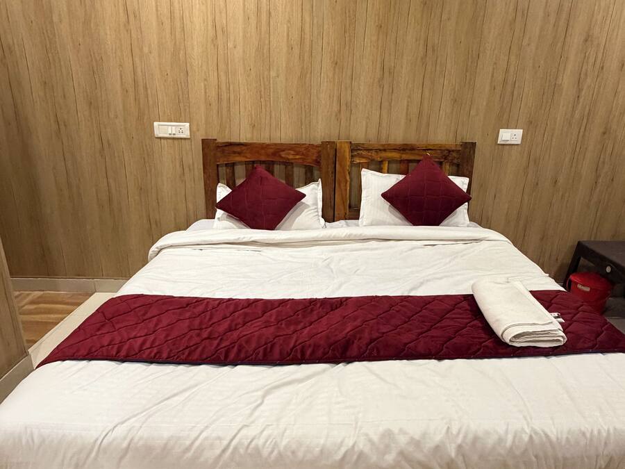 A bed with a wooden headboard, white bedding, and a red quilted blanket.