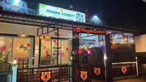 Um edifício com uma placa indicando 'MAGPIE CORBETT' e um grande letreiro iluminado sobre a entrada.