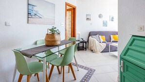 Uma sala de estar moderna com uma mesa de jantar de vidro, cadeiras verdes, um sofá com almofadas, um armário verde e uma pintura na parede.