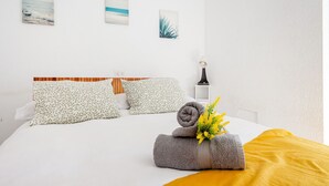 Cama bem arrumada com almofadas estampadas, uma toalha enrolada e um cobertor amarelo.