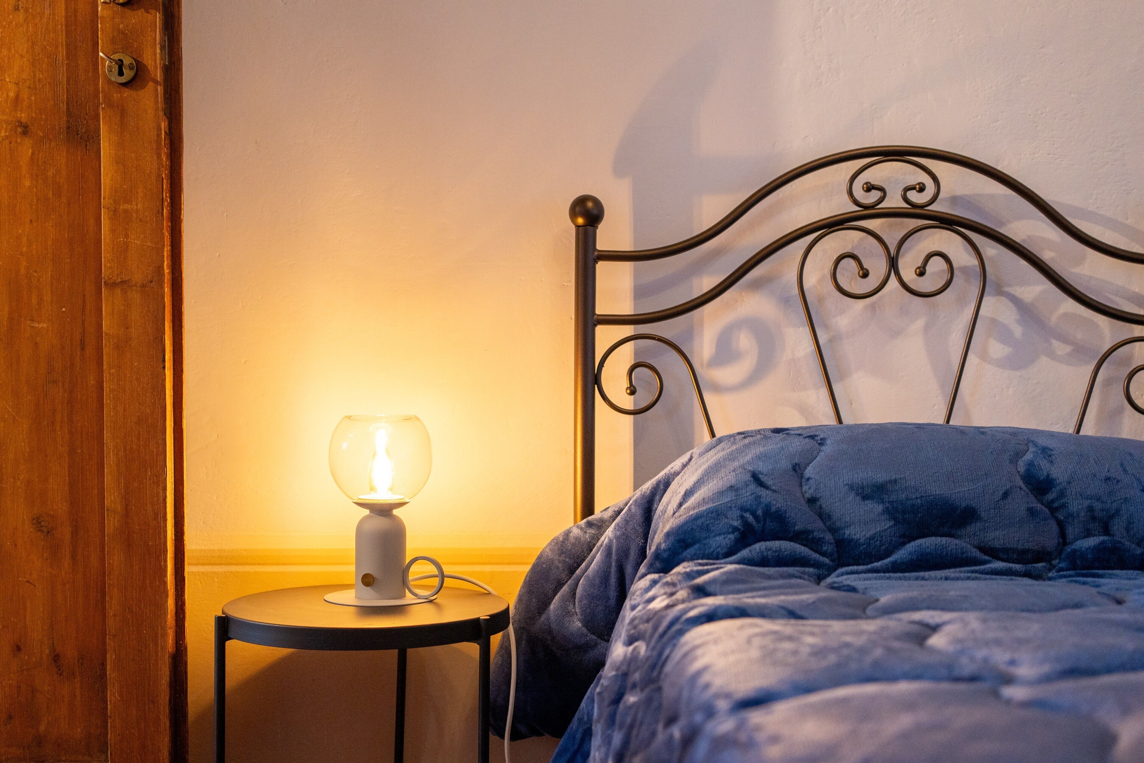 A bed with a metal headboard, a bedside table with a lamp, and a wooden door.