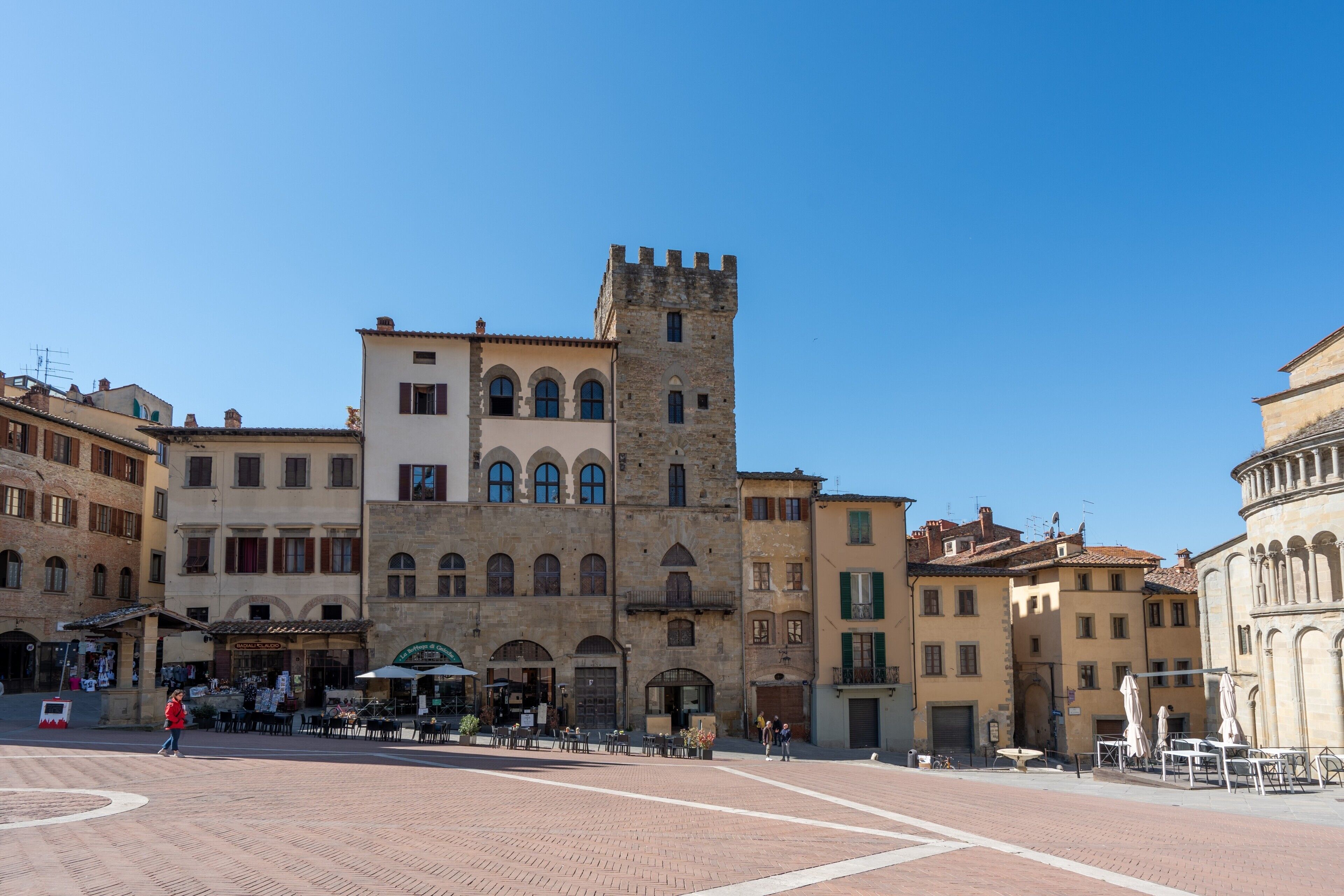 A historic square with a prominent tower, traditional buildings, and outdoor seating areas.