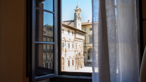 A window with a view of a building with a clock tower, balconies, and a clear sky.