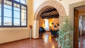 An interior with a tiled floor, a large window, an arched doorway, a potted plant, and a seating area with a lamp.