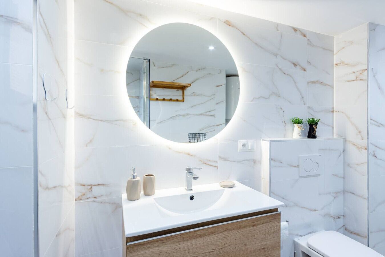 A modern bathroom with a marble vanity, a round mirror, and a toilet.