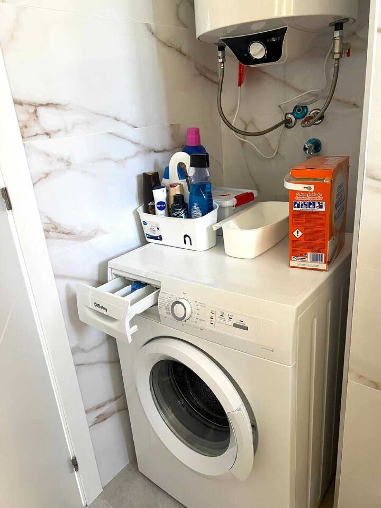 Un espace buanderie compact comprenant un lave-linge à chargement frontal, un étendoir et une boîte de rangement contenant des produits de nettoyage.