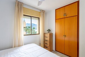 A bedroom with a bed, a window with curtains, a wooden wardrobe, and a dresser. - Relax Tropical Almuñecar (Almuñécar)