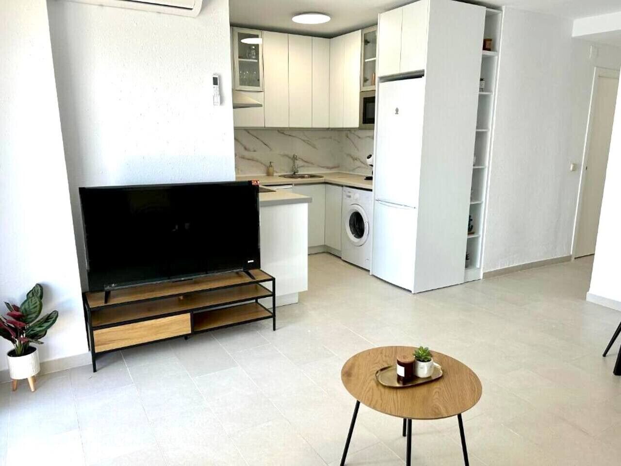 A modern kitchen with a built-in washing machine, a flat-screen TV, and a small dining table.