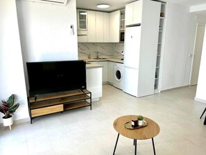 A modern kitchen with a built-in washing machine, a flat-screen TV, and a small dining table. - Brisa Marina Almuñecar playa de velilla (Velilla-Taramay)