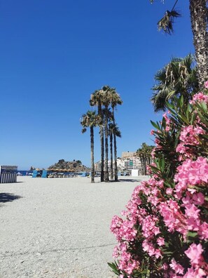 A beach with palm trees, a clear sky, and a building in the background. - Refugio del mar Almuñecar (Almuñécar)