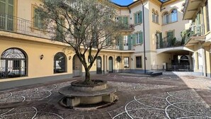 A courtyard with a central tree, patterned paving, and multi-story buildings with balconies. - Loft @ Veratti by iCasamia .it (Varese)
