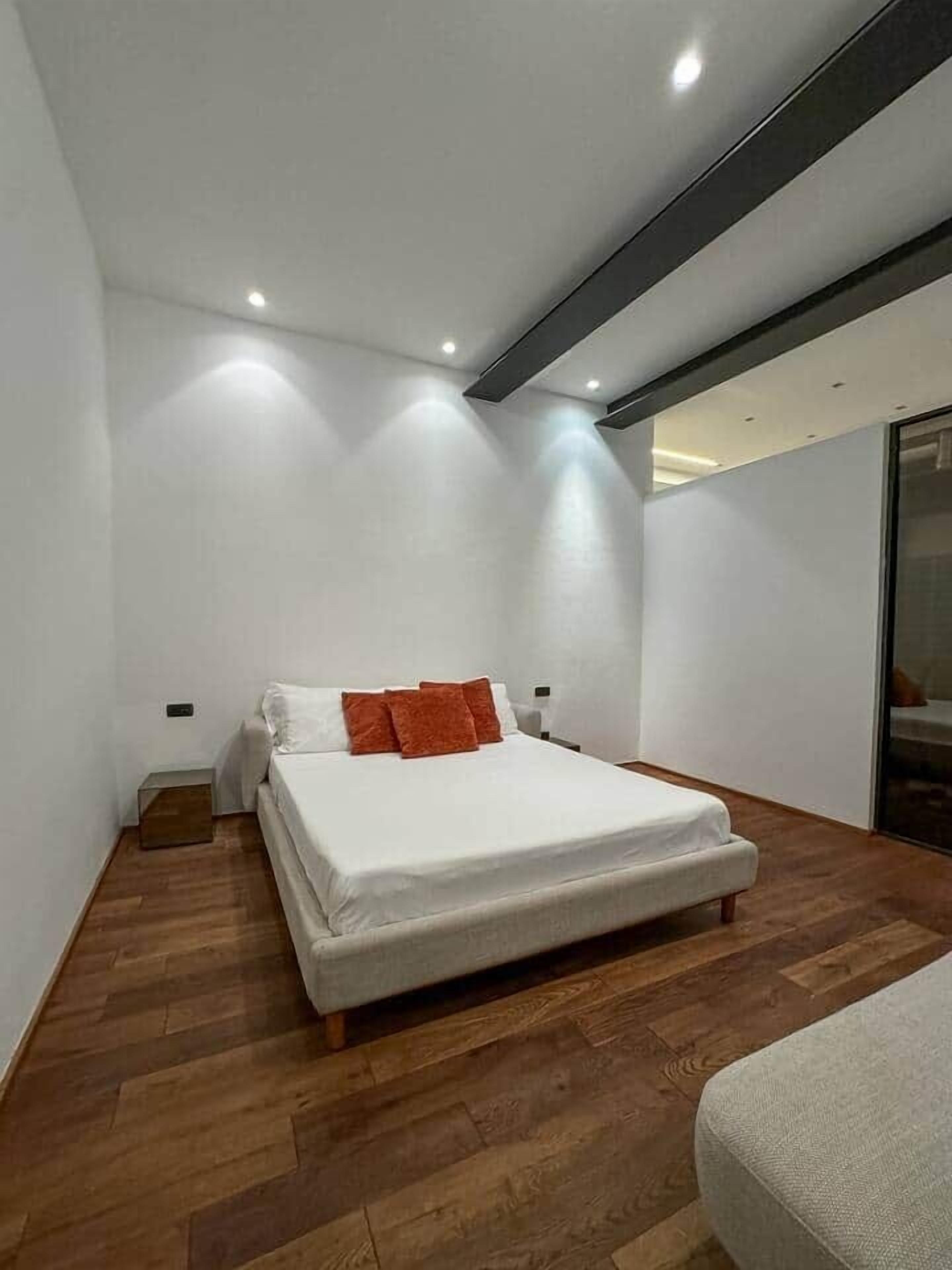 A modern bedroom with a bed, wooden flooring, and recessed ceiling lights.