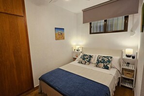 A bedroom with a bed, bedside tables, a nightstand, a window with blinds, a door, and a small painting on the wall. - Almuñecar / Velilla Sea View (Almuñécar)