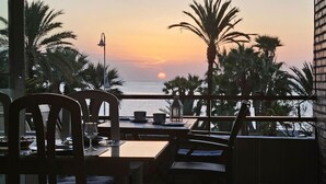 Un espace repas offrant une vue sur le coucher de soleil sur l’océan, entouré de palmiers.