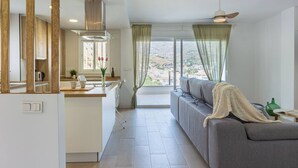 Een moderne keuken met een centraal eiland, een zithoek met een bank en een groot raam met gordijnen.
