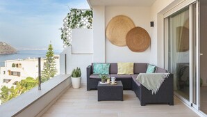 Een balkon met een bank, bijzettafeltje en planten in potten.