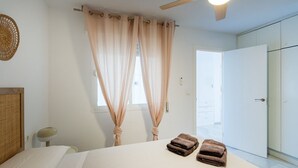 Een slaapkamer met een bed, twee handdoeken, een plafondventilator en een raam met gordijnen.