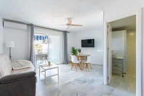 A modern living room with a sofa, a dining table with chairs, a ceiling fan, and a TV mounted on the wall. - Apartamento Portisol Velilla (Velilla-Taramay)