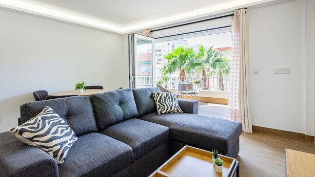 A modern living room with a sectional sofa, a coffee table with a plant, and a balcony with palm trees. - Esencia Marina la Najarra (Almuñécar)
