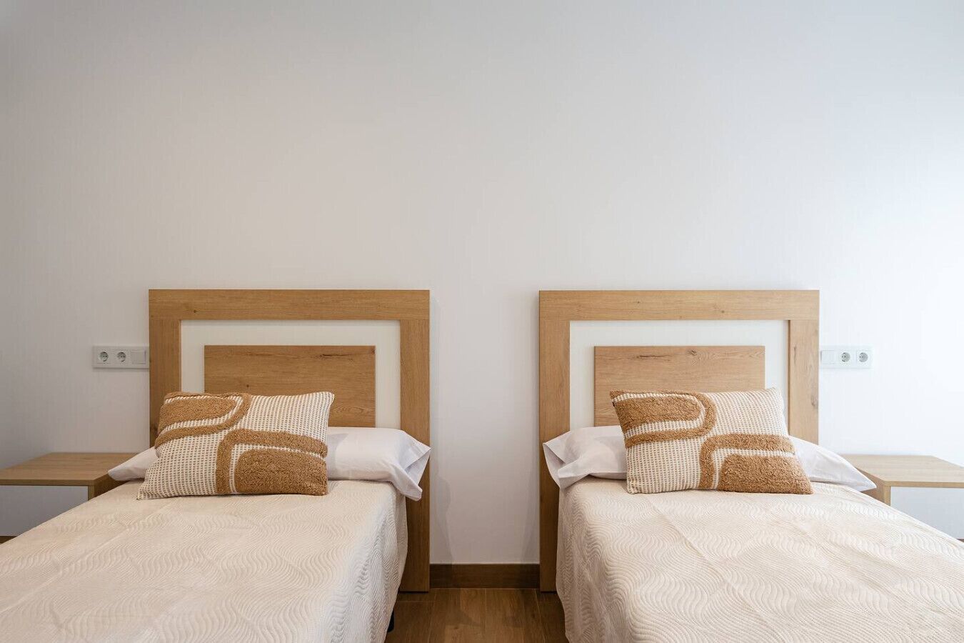 Two twin beds with wooden headboards, white bedding, and patterned pillows.