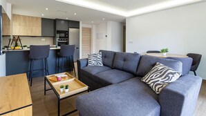 A modern living room with a grey sofa, two armchairs, a wooden coffee table, and a kitchen area in the background. - Esencia Marina la Najarra (Almuñécar)