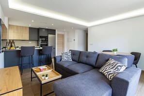 A modern living room with a grey sofa, two armchairs, a wooden coffee table, and a kitchen area in the background. - Esencia Marina la Najarra (Almuñécar)