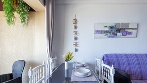 A dining area with a table set for two, a white chair, a sofa, and a wall-mounted art piece. - Mar y calma Chinasol Almuñecar (Almuñécar)